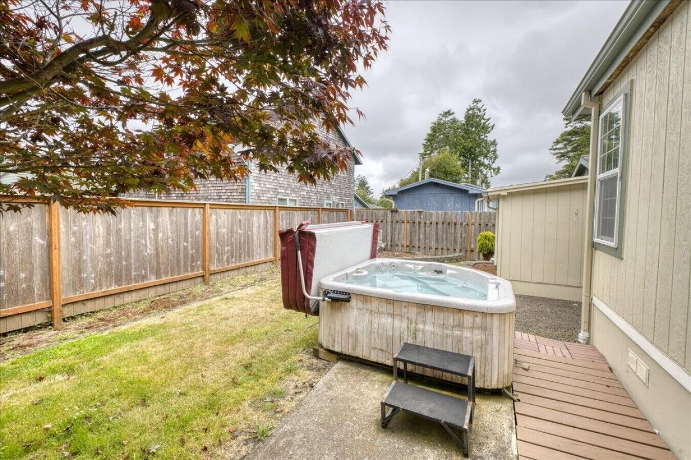 A backyard with a hot tub, a wooden deck, and a fenced area.