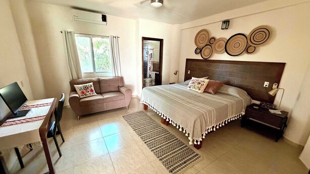 Um quarto com cama, escrivaninha com computador, sofá e ventilador de teto.