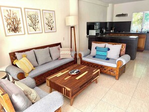 Ein Wohnzimmer mit Sofa, Sessel, Couchtisch und einem Kunstwerk an der Wand.