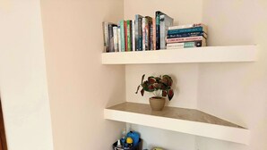 Uma estante de canto com livros, uma planta em vaso e uma caixa organizadora.