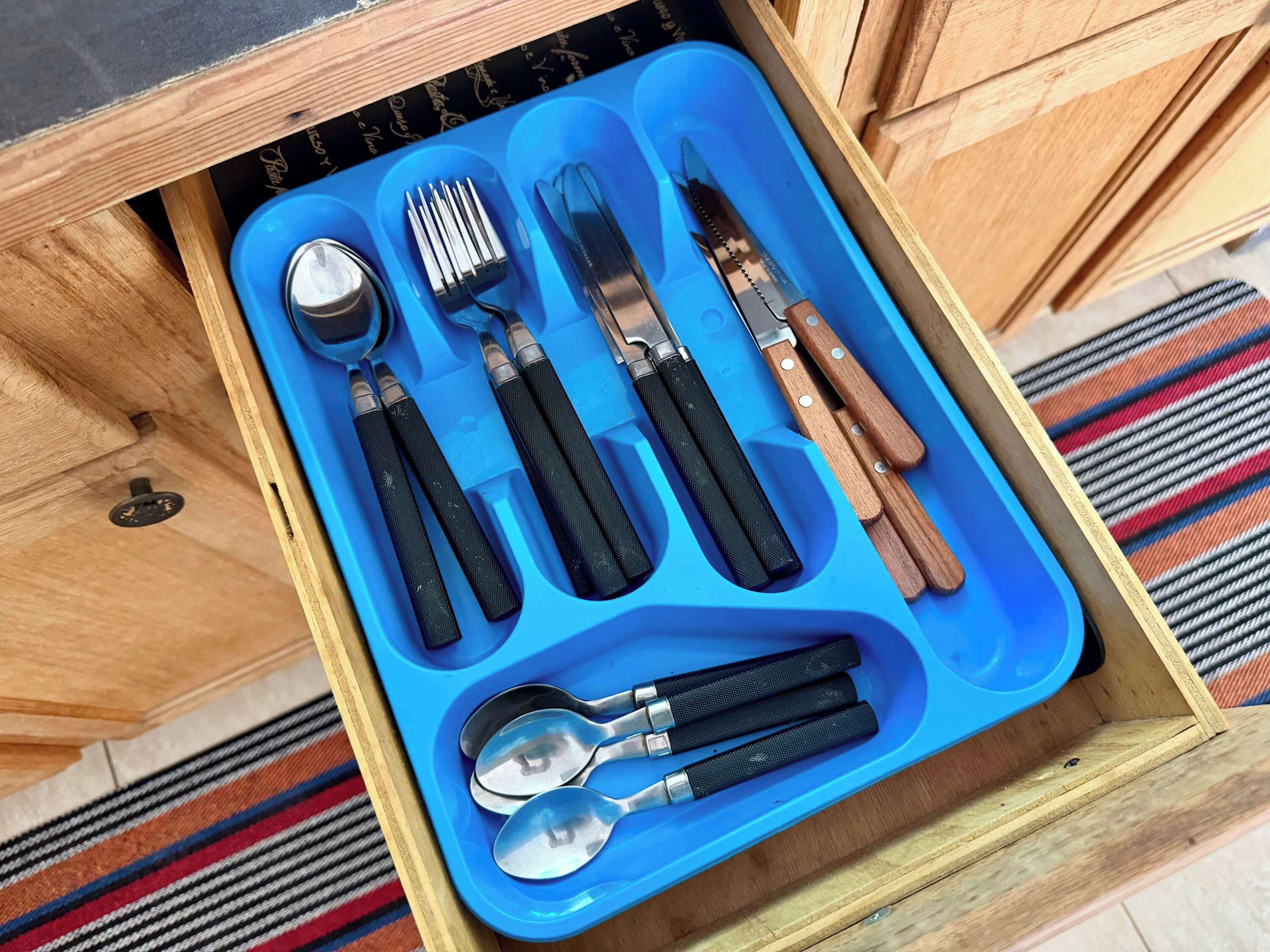 Un cassetto foderato di blu con diversi utensili, tra cui cucchiai, forchette e coltelli.