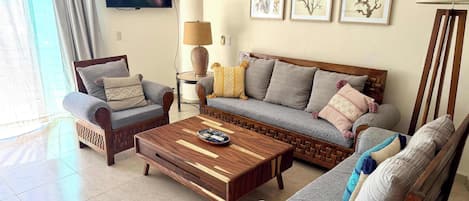 A living room with a sofa, two armchairs, a coffee table, a TV, and wall art.