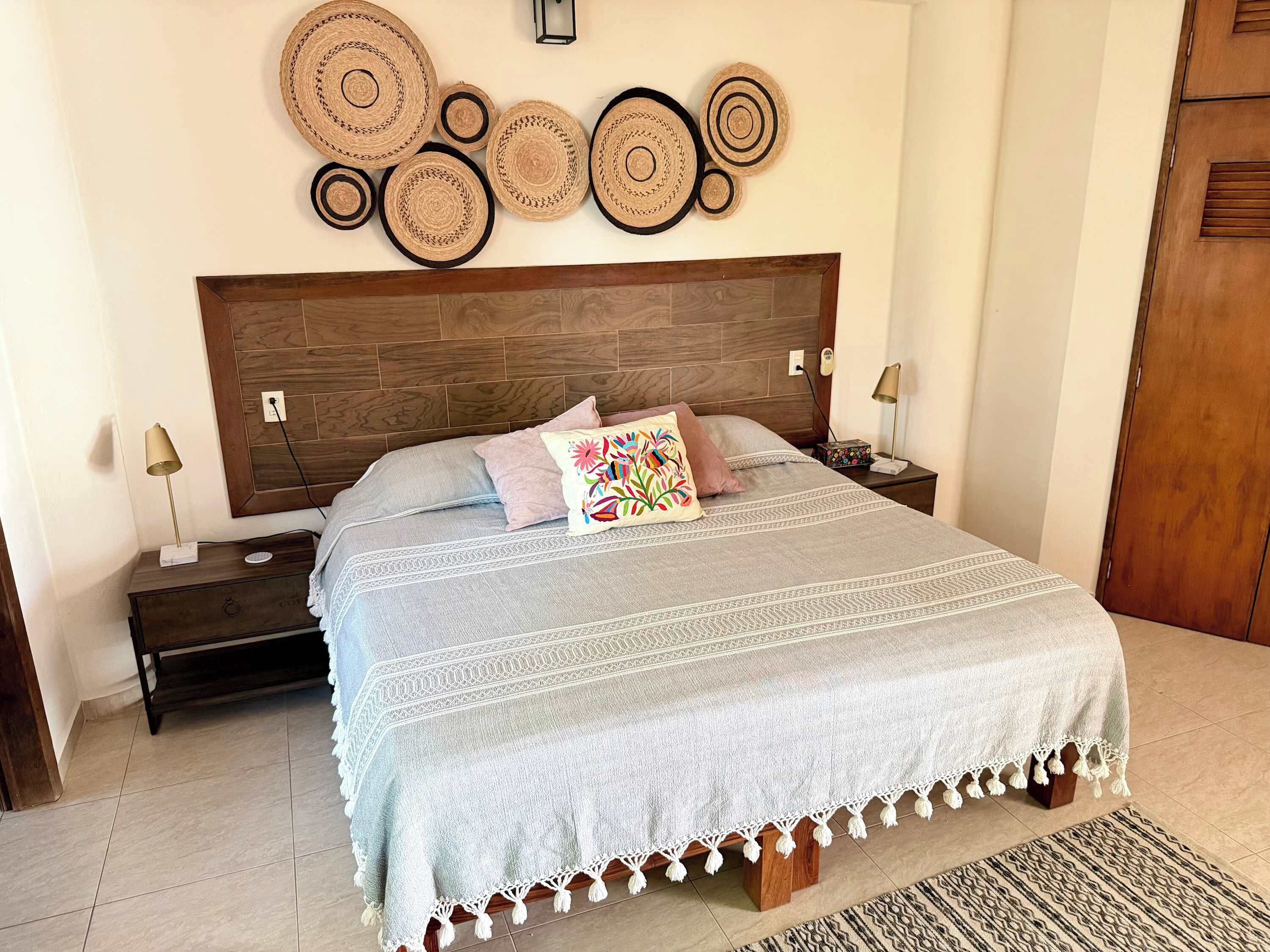 Un dormitorio ordenado con cabecera de madera, colcha estampada y un adorno decorativo en la pared.