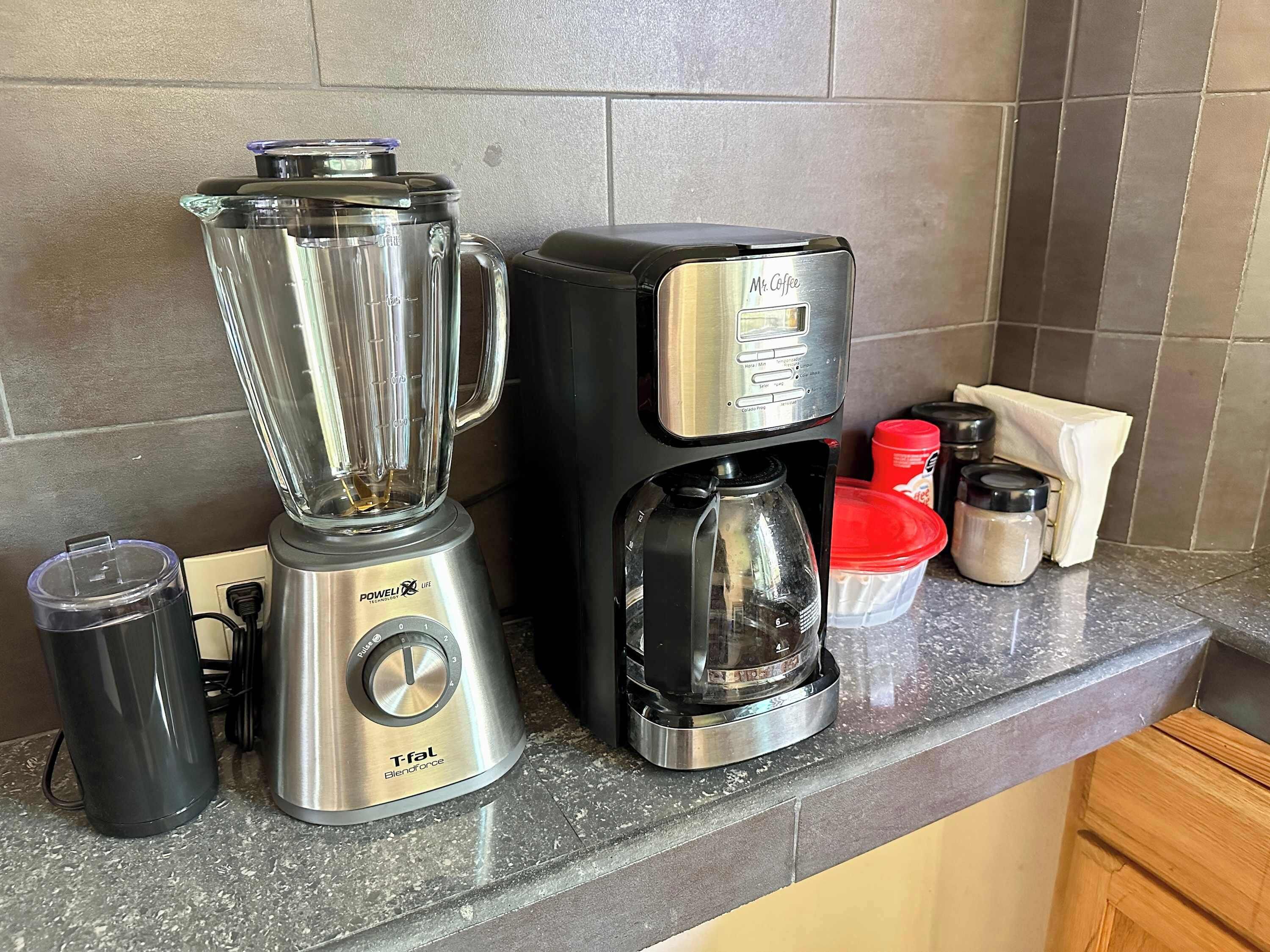 Eine Küchenarbeitsfläche mit einem Mixer, einer Kaffeemaschine und einem Thermosbehälter.