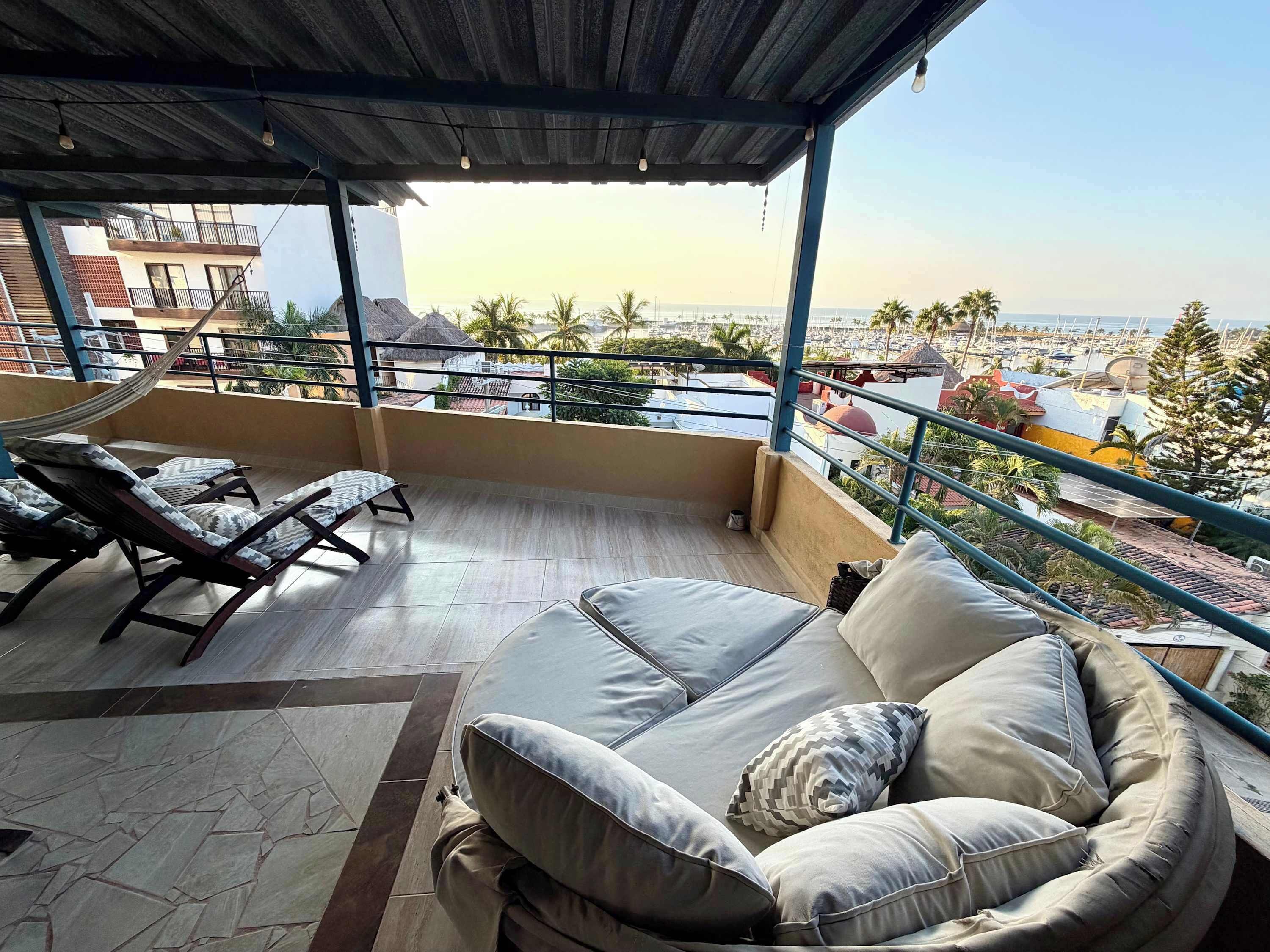 Un balcon avec un canapé et des fauteuils, offrant une vue sur le paysage urbain et les palmiers.