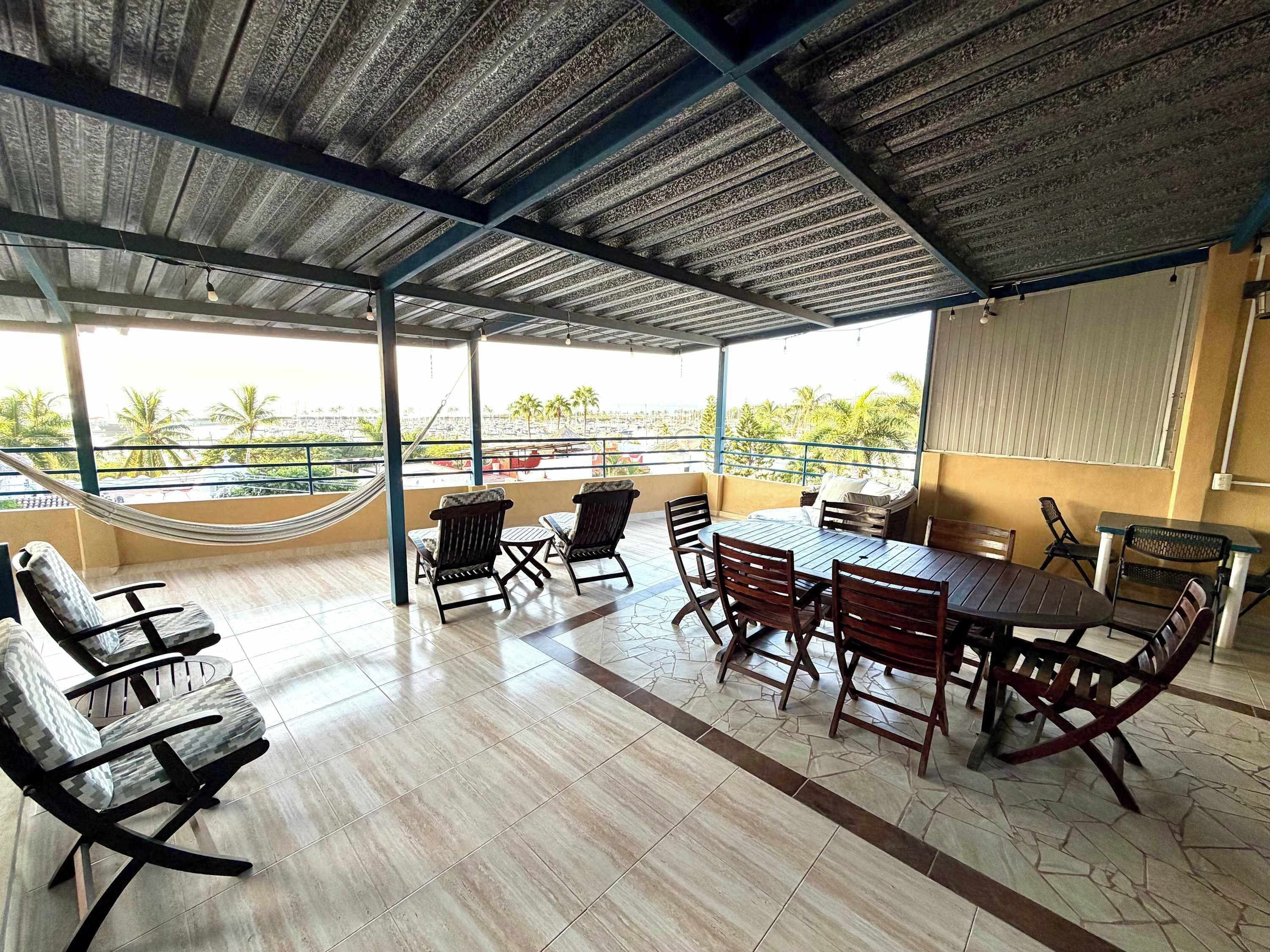 A covered outdoor seating area with a view of palm trees and a cityscape.