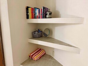 A corner with two white shelves; the top shelf holds books and a decorative item, the bottom shelf has a folded towel and a small basket with toiletries. - Rooftop Patio, Marina Views––1 Block to Beach (La Cruz de Huanacaxtle)