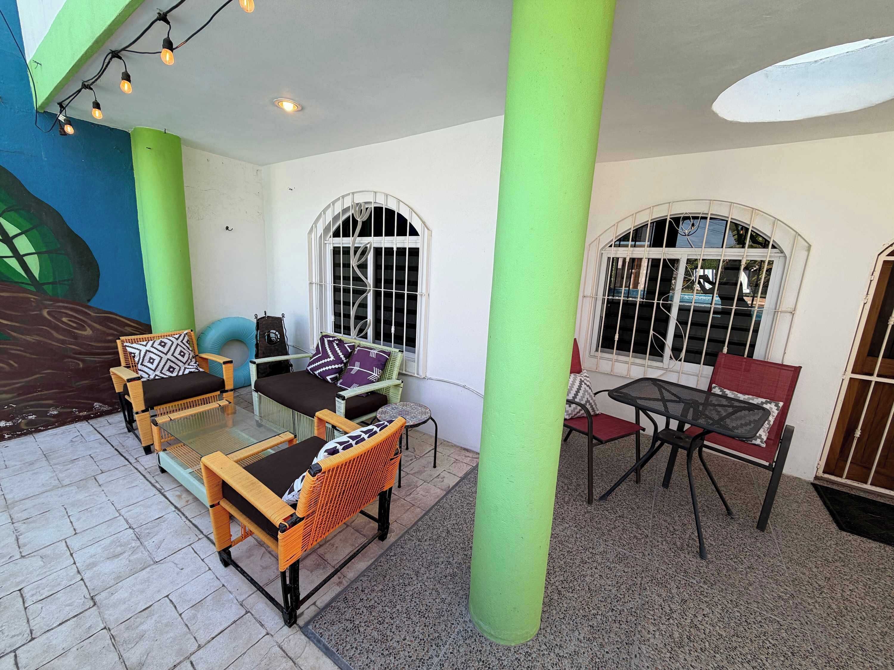 A covered outdoor seating area with wicker furniture, a small table, and a mural on the wall.