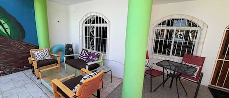 A covered outdoor seating area with wicker furniture, a small table, and a mural on the wall.