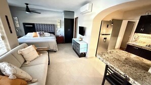 Quarto de hotel moderno com uma cama, área de estar com sofá, espaço para refeições com bar e cozinha compacta.