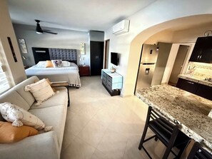 Ein modernes Hotelzimmer mit einem Bett, einer Sitzecke mit einer Couch, einem Essbereich mit einer Bar und einer Küchenzeile.