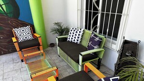 Uma área de pátio com móveis de vime, um sofá verde e uma janela com grades de metal.