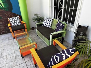 Ein Patio mit Korbmöbeln, einem grünen Sofa und einem Fenster mit Metallgitter.