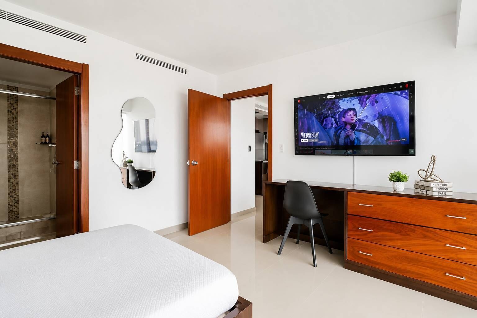 A modern hotel room with a bed, a desk, a television, and a bathroom.