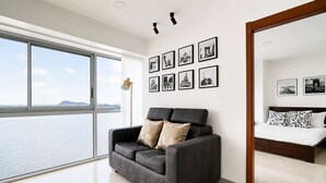 Een moderne woonkamer met een groot raam, een bank, een bed en een wand met ingelijste foto's.