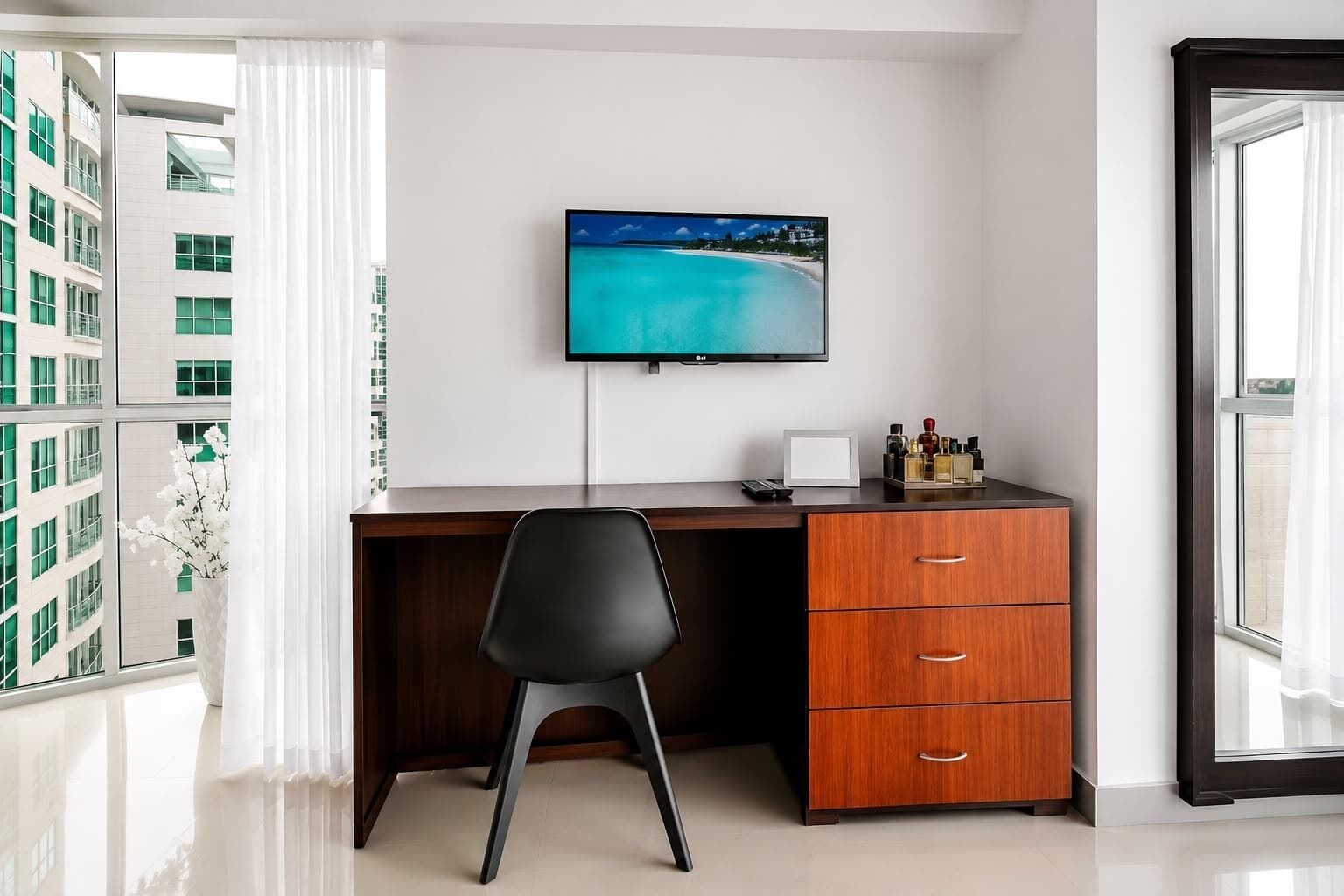 A modern hotel room with a desk, chair, and a flat-screen TV mounted on the wall.