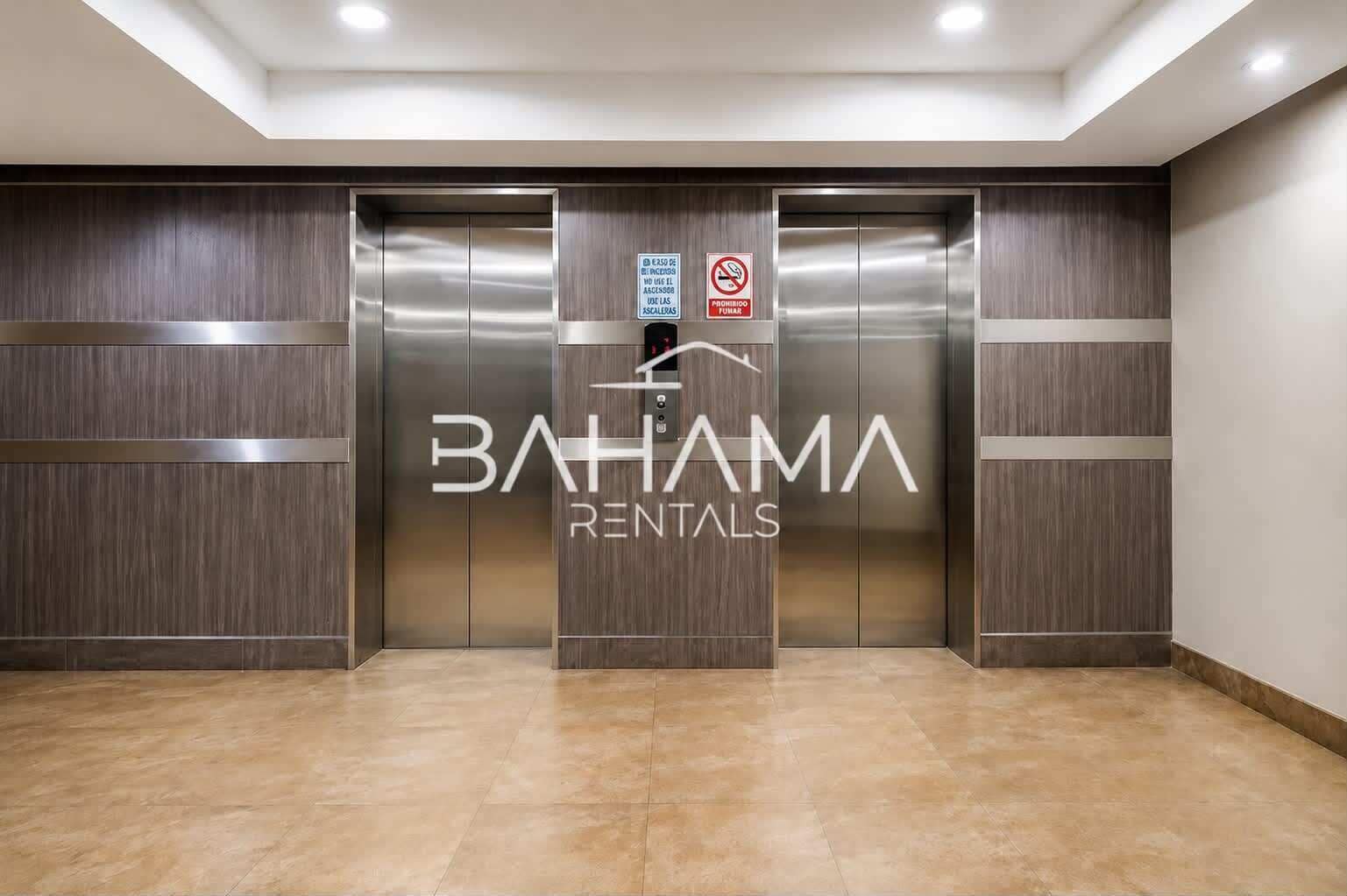 A modern elevator with a metallic finish and a logo for 'BAHAMA RENTALS' on the wall.