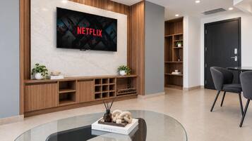 A modern living room with a flat-screen TV mounted on a wooden wall, a glass coffee table, and a seating area with chairs.