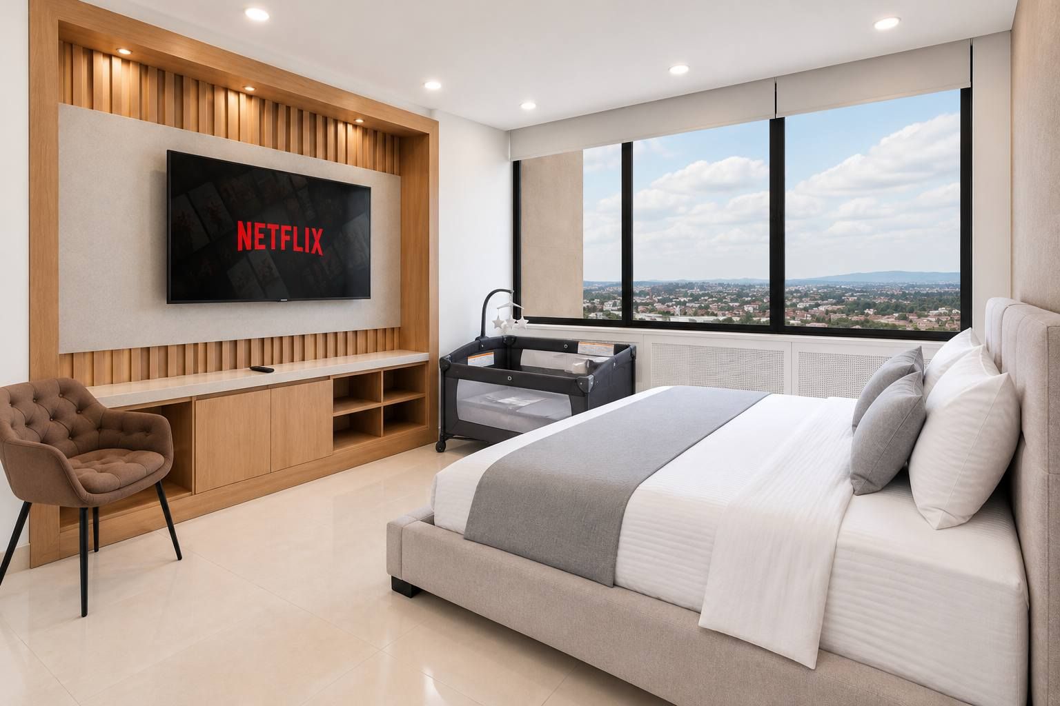 Ein modernes Schlafzimmer mit einem großen Bett, einem an der Wand befestigten Fernseher, einem Schreibtisch und Blick auf die Stadt durch große Fenster.