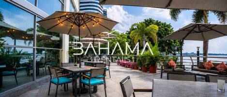 An outdoor seating area with tables and chairs, umbrellas, and potted plants.