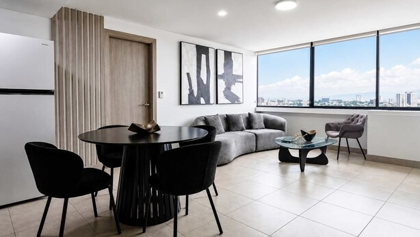 Una sala de estar moderna con comedor, un sofá gris, una mesa de centro y un amplio ventanal con vista a la ciudad.