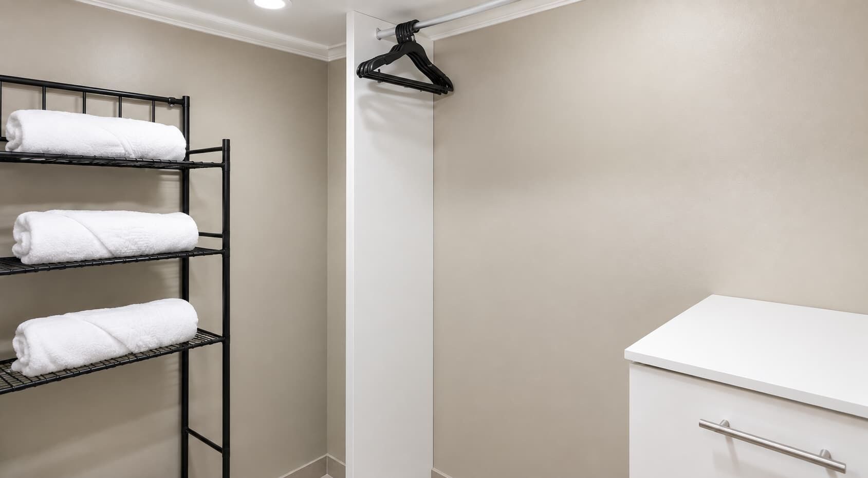 A bathroom with a towel rack holding three towels, a shower area, and a white sink with a cabinet.