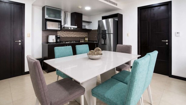 Una cocina moderna con una isla central, una mesa de comedor con sillas y un refrigerador.