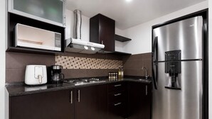 Una cocina moderna con armarios oscuros, un refrigerador de acero inoxidable, una cafetera y un microondas integrado.