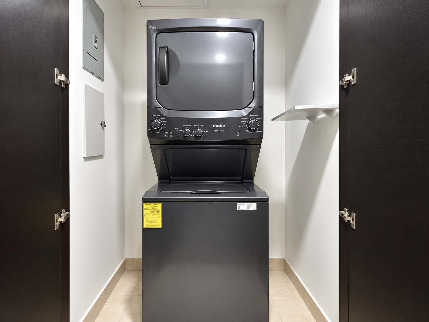A compact washer and dryer unit with a control panel, placed in a narrow hallway with dark doors.