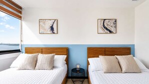 Habitación de hotel con dos camas, vista al mar y arte abstracto en las paredes.