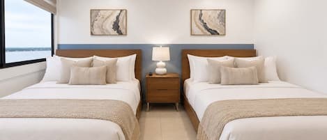 Una camera d'albergo con due letti, un comodino con una lampada e opere d'arte alle pareti.