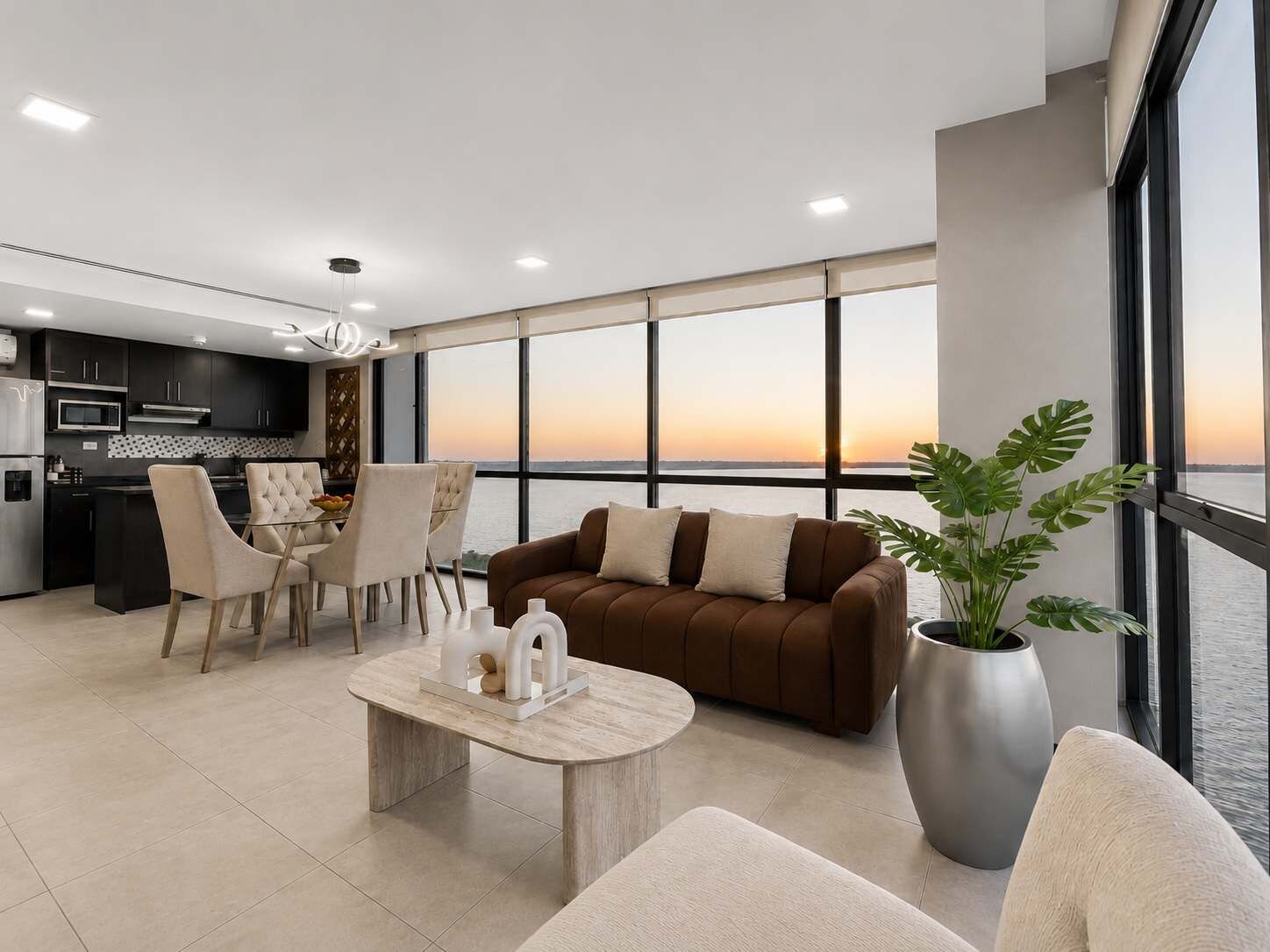 Ein modernes Wohnzimmer mit einer Couch, Sesseln, einem Couchtisch und einem großen Fenster mit Sonnenuntergangsblick.