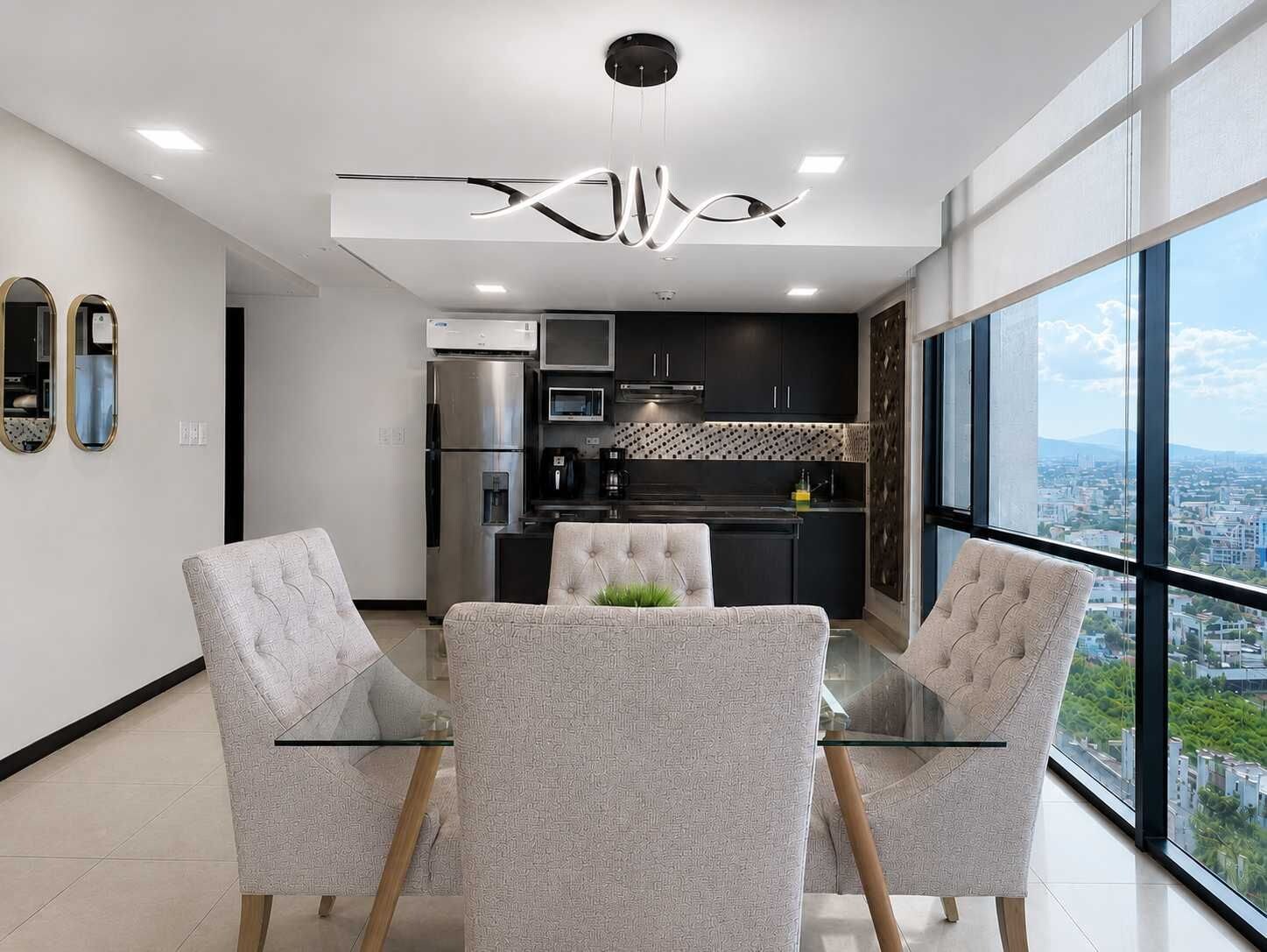 Eine moderne Küche mit Edelstahlgeräten, einem Glastisch mit Stühlen und Blick auf die Stadt durch große Fenster.