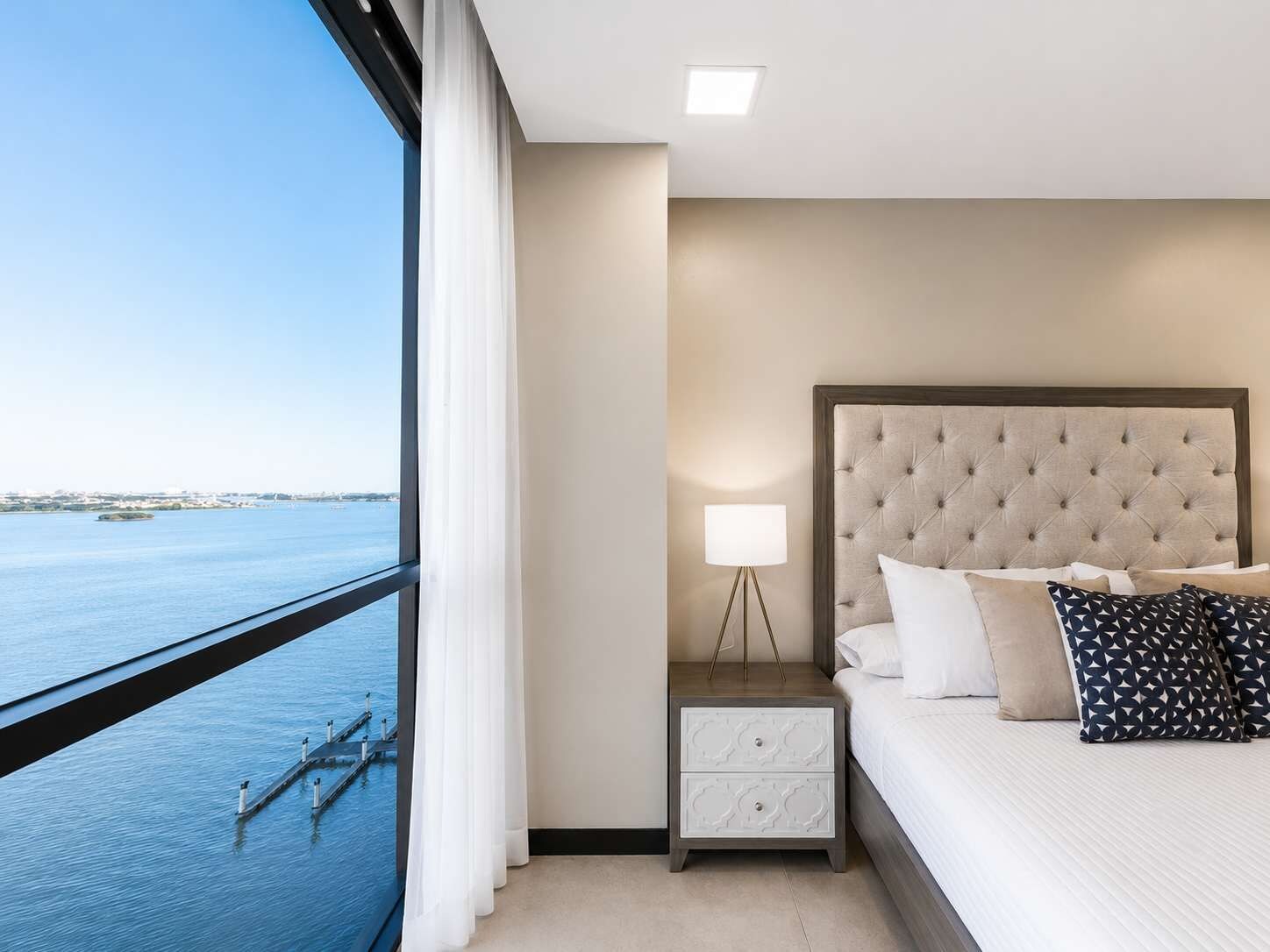 Ein Hotelzimmer mit Bett, Nachttisch, Lampe und Blick auf das Wasser.