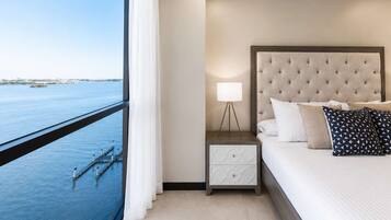 Ein Hotelzimmer mit Bett, Nachttisch, Lampe und Blick auf das Wasser.