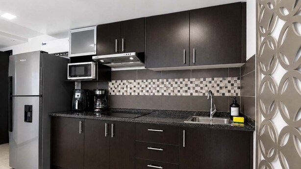 Una cocina moderna con muebles oscuros, un refrigerador de acero inoxidable, un microondas y una cafetera.