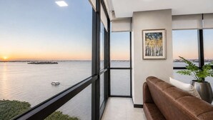 Un interior moderno con un amplio ventanal que ofrece vistas a un cuerpo de agua y un atardecer.