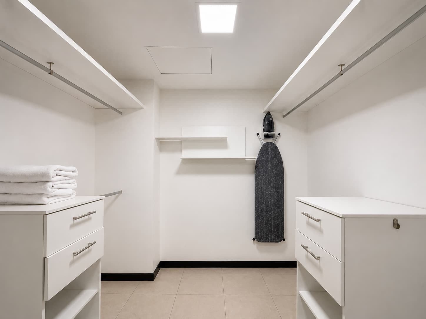 Un baño moderno y limpio, con muebles blancos, una pila de toallas y un tablero de planchar adosado a la pared.
