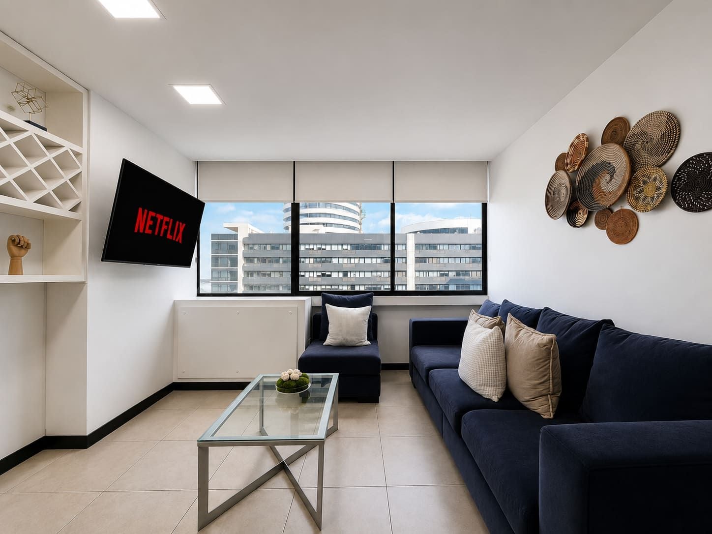 A modern living room with a glass coffee table, a dark sofa, and a wall-mounted TV displaying 'NETFLIX'.