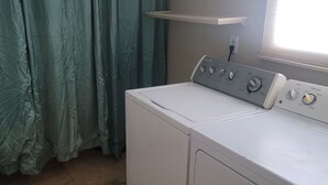 A laundry area with a front-loading washer and dryer, a window with blinds, and a curtain. - Marvelous 3-bedroom house with AC big Pool and Jaccuzi very quiet in Lehigh Acre (Lehigh Acres)