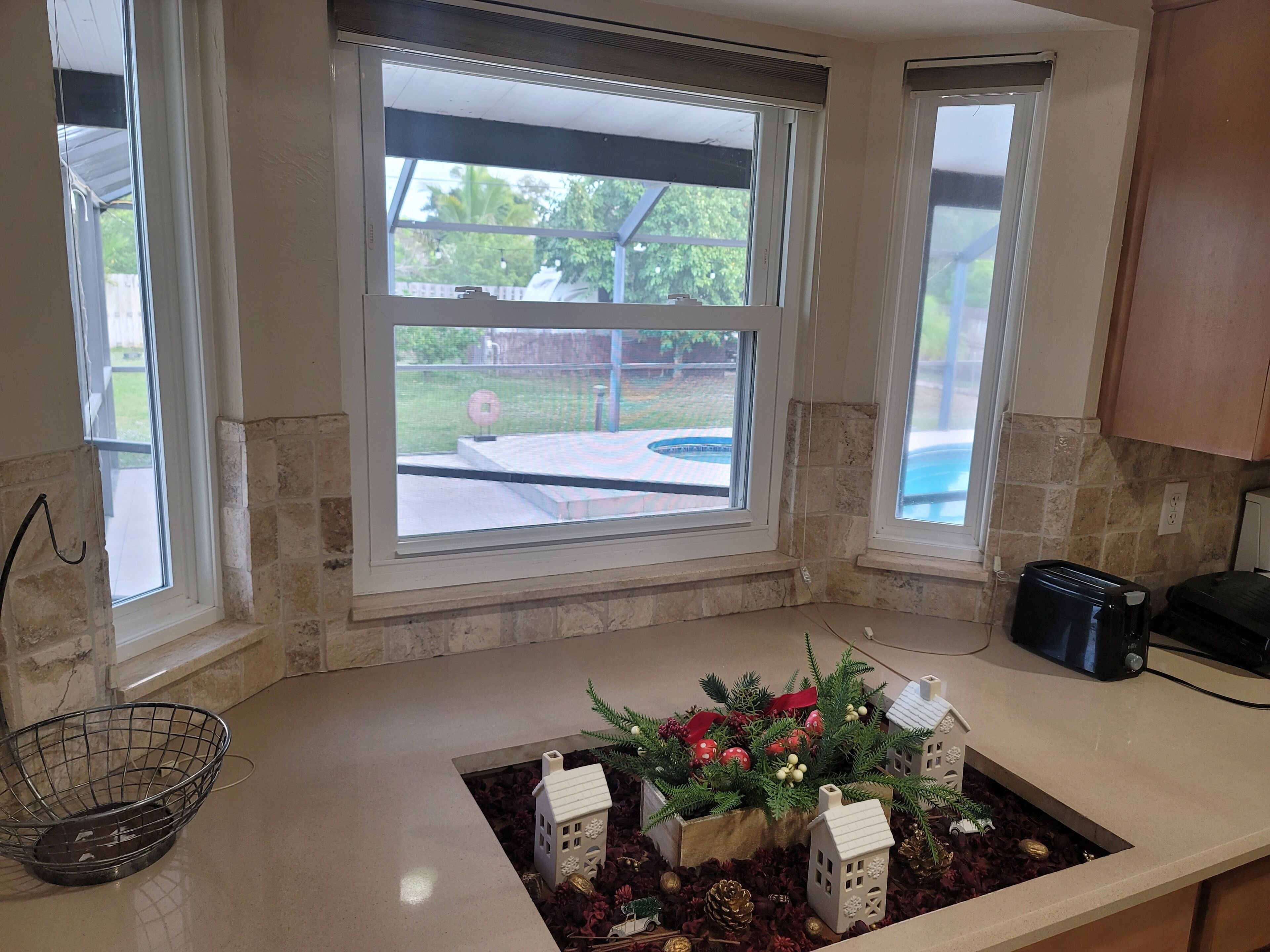 Una cocina con ventana que da a un patio trasero, una encimera con un arreglo decorativo y un tostador.