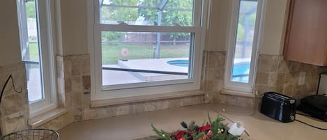 A kitchen with a window overlooking a backyard, a countertop with a decorative arrangement, and a toaster.
