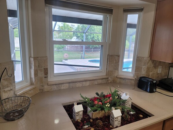 A kitchen with a window overlooking a backyard, a countertop with a decorative arrangement, and a toaster.