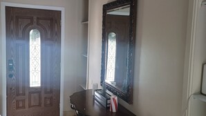 A hallway with a wooden door, a dark wooden console table, a mirror, and a light switch on the wall. - Marvelous 3-bedroom house with AC big Pool and Jaccuzi very quiet in Lehigh Acre (Lehigh Acres)