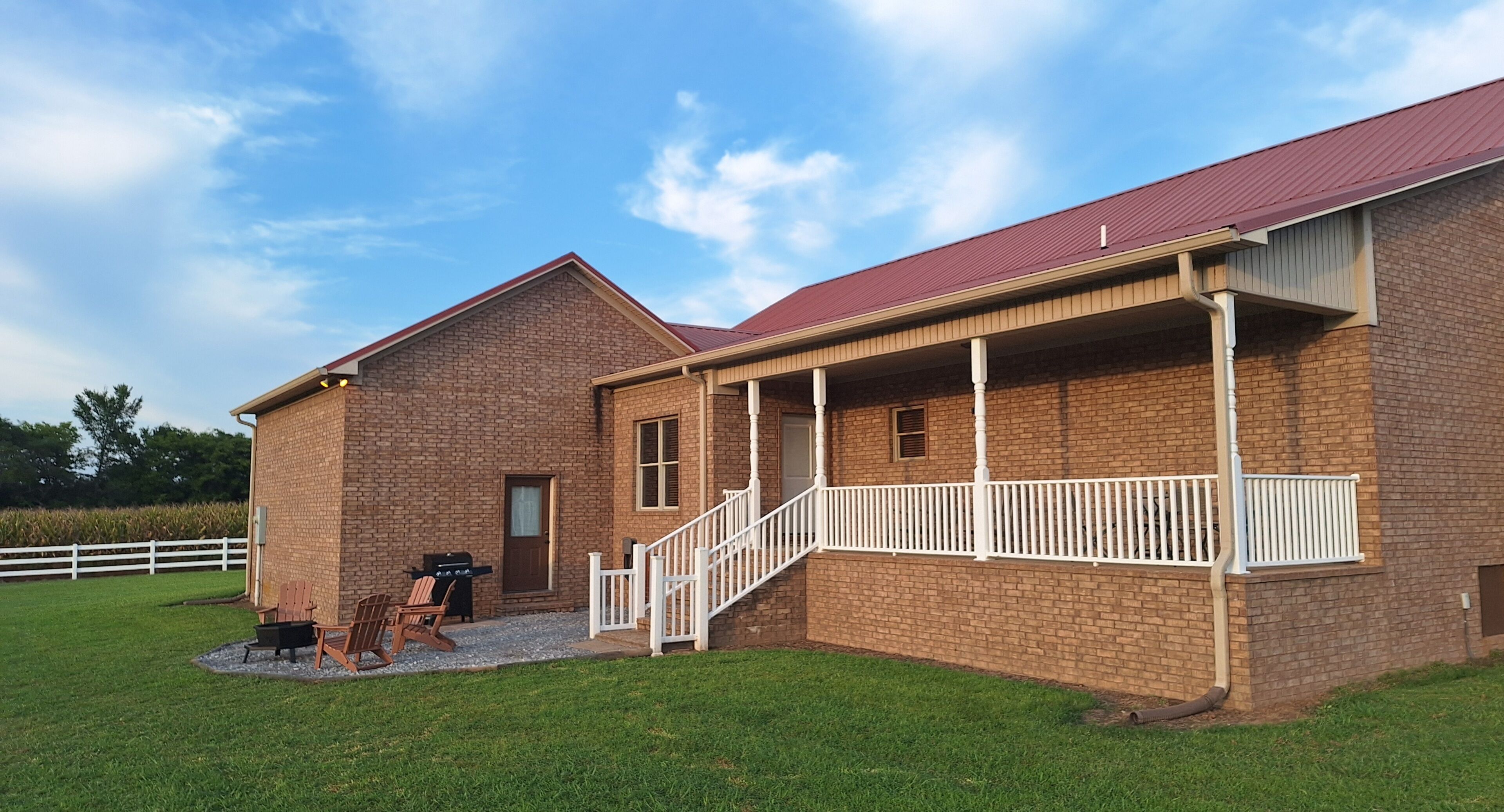 A brick building with a red roof, a covered porch, and a white fence in the background.