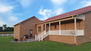 A brick building with a red roof, a covered porch, and a white fence in the background.
