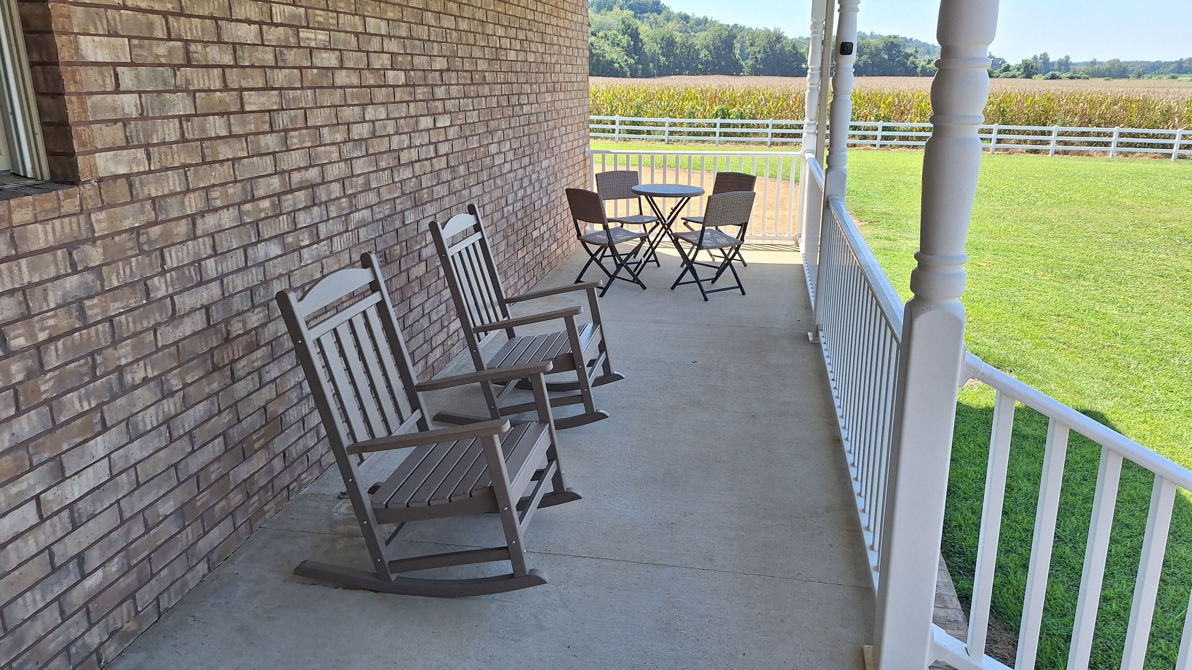 A brick building with a porch featuring rocking chairs and a table.