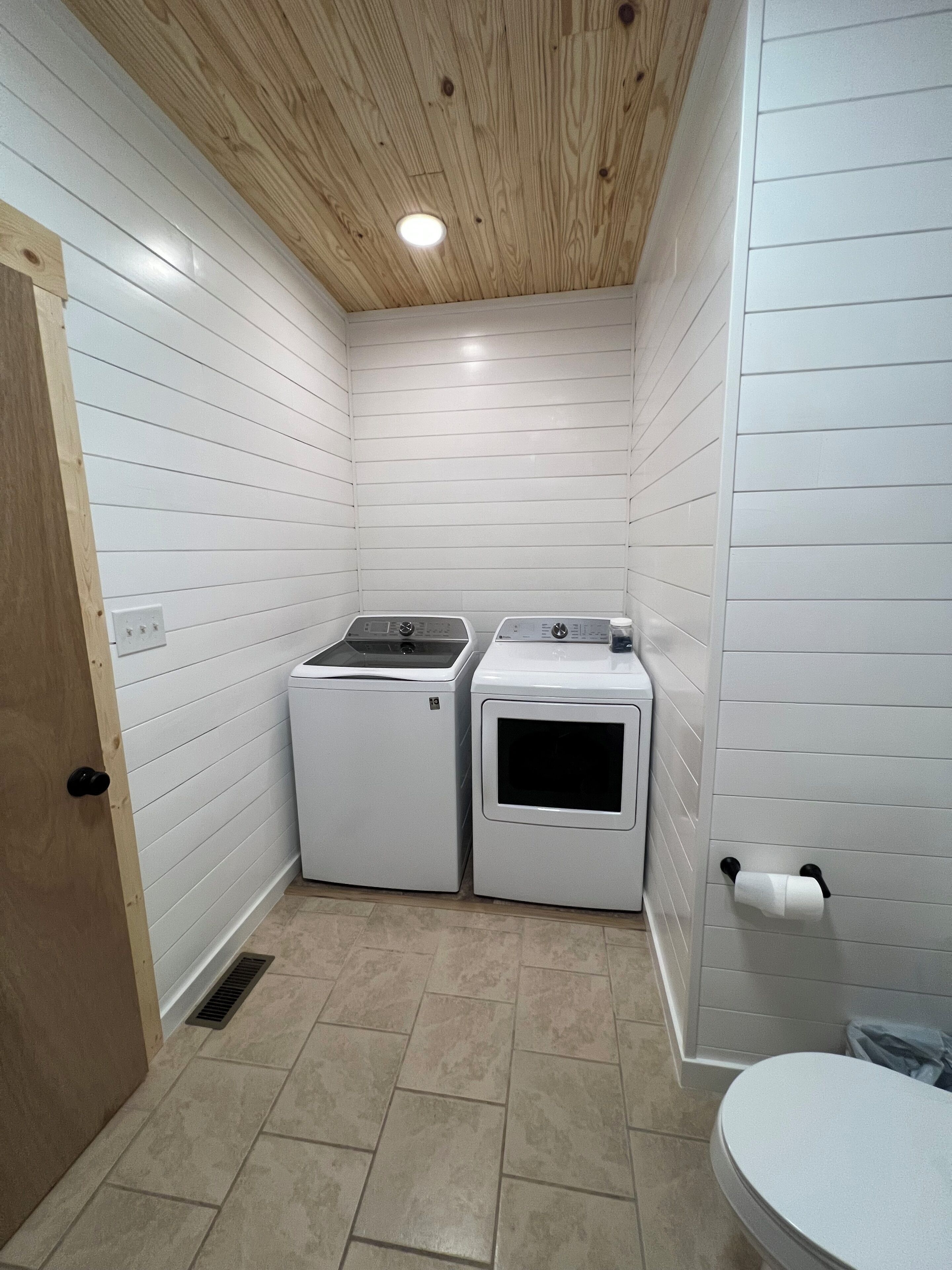 A laundry room with two washing machines, a wooden ceiling, and a tiled floor.