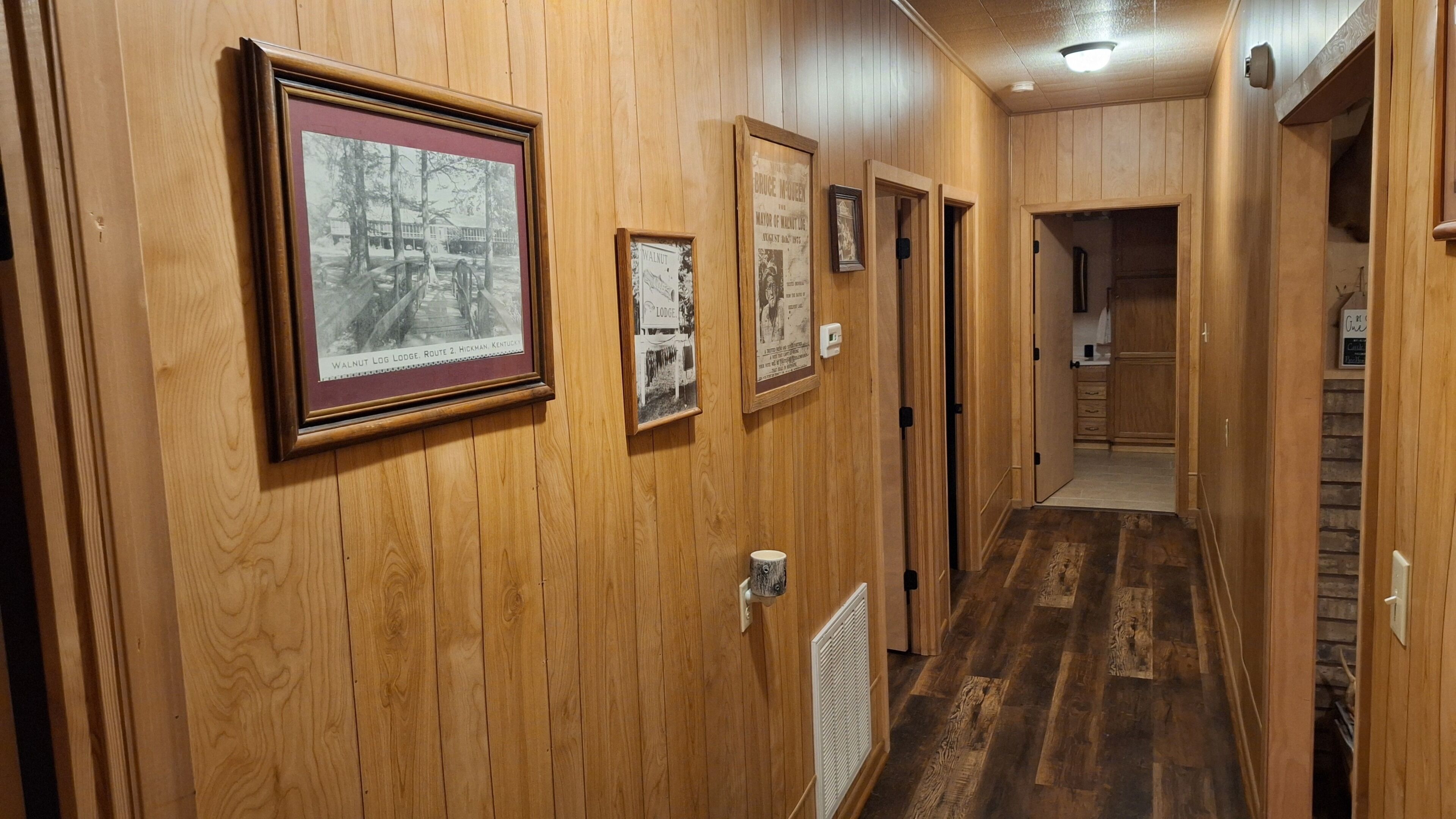 Un pasillo de madera con fotografías históricas enmarcadas en la pared, un radiador y una puerta que da a una habitación.