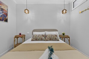 Une chambre à coucher avec un lit, deux tables de chevet, un tableau au mur et deux lampes suspendues.
